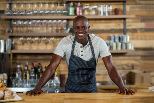 Portrait of smiling waiter standing at counter in cafÃ©